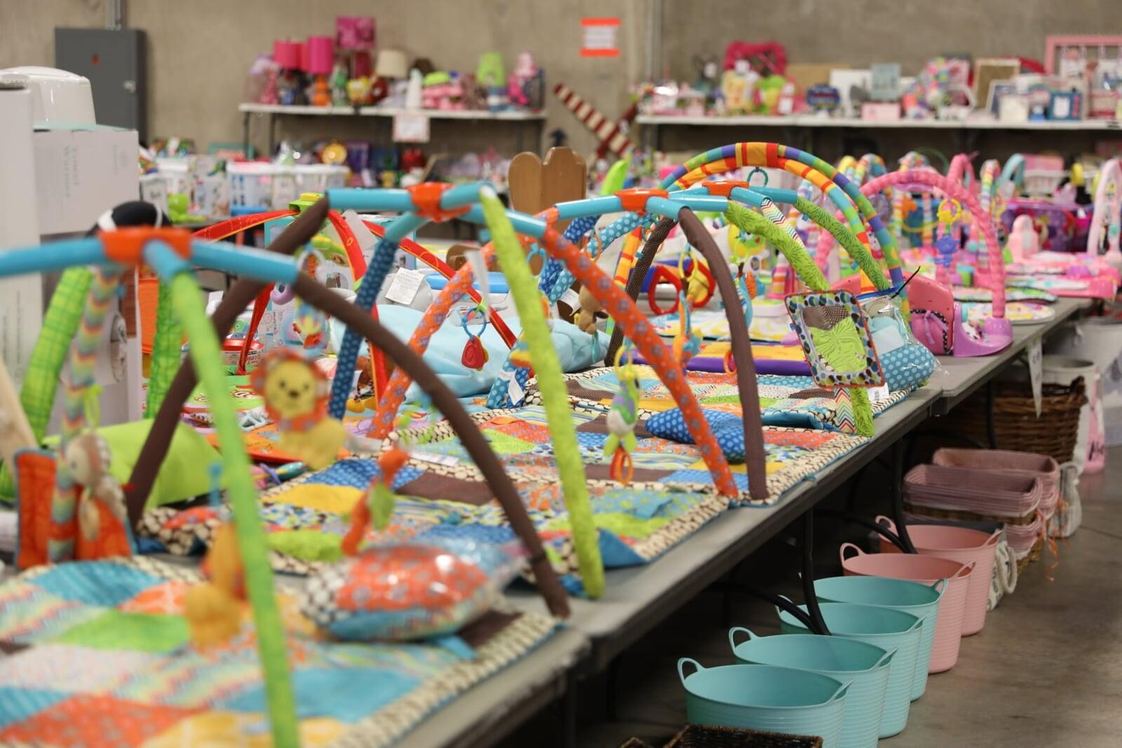 Tricycles, scooters and toys lined up on a table waiting for shoppers to attend the sale.